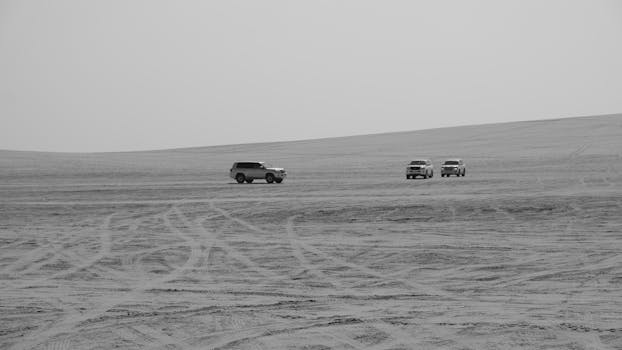 Monochrome shot of SUVs navigating the vast, sandy desert near Doha, Qatar.