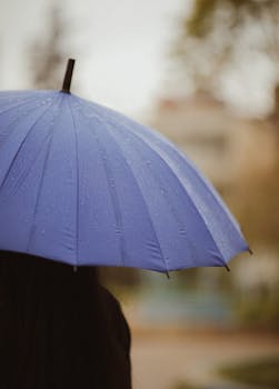 Detailed close-up of raindrops on a blue umbrella in a rainy outdoor setting.