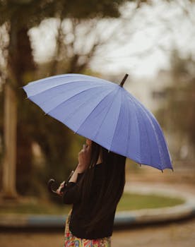 Woman holding a blue umbrella in a rainy park setting, capturing the essence of a rainy day.