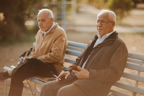 Free Two senior men sitting on a bench outdoors, enjoying a casual moment. Stock Photo
