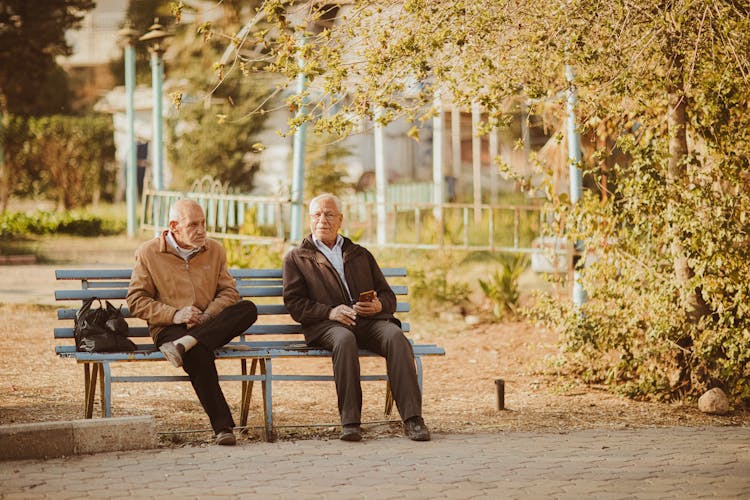 Two Old Men Sitting On Bench In Park In Autumn