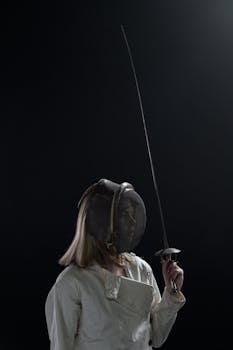 Dramatic portrait of a female fencer holding a sword in a dark studio setting.
