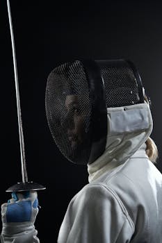 Focused fencer in sports gear with sword during a studio shoot, emphasizing strength and agility.