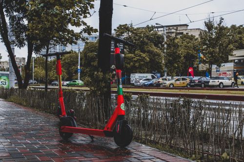 Free A vibrant red electric scooter parked on a wet sidewalk in Bucharest, showcasing urban mobility. Stock Photo