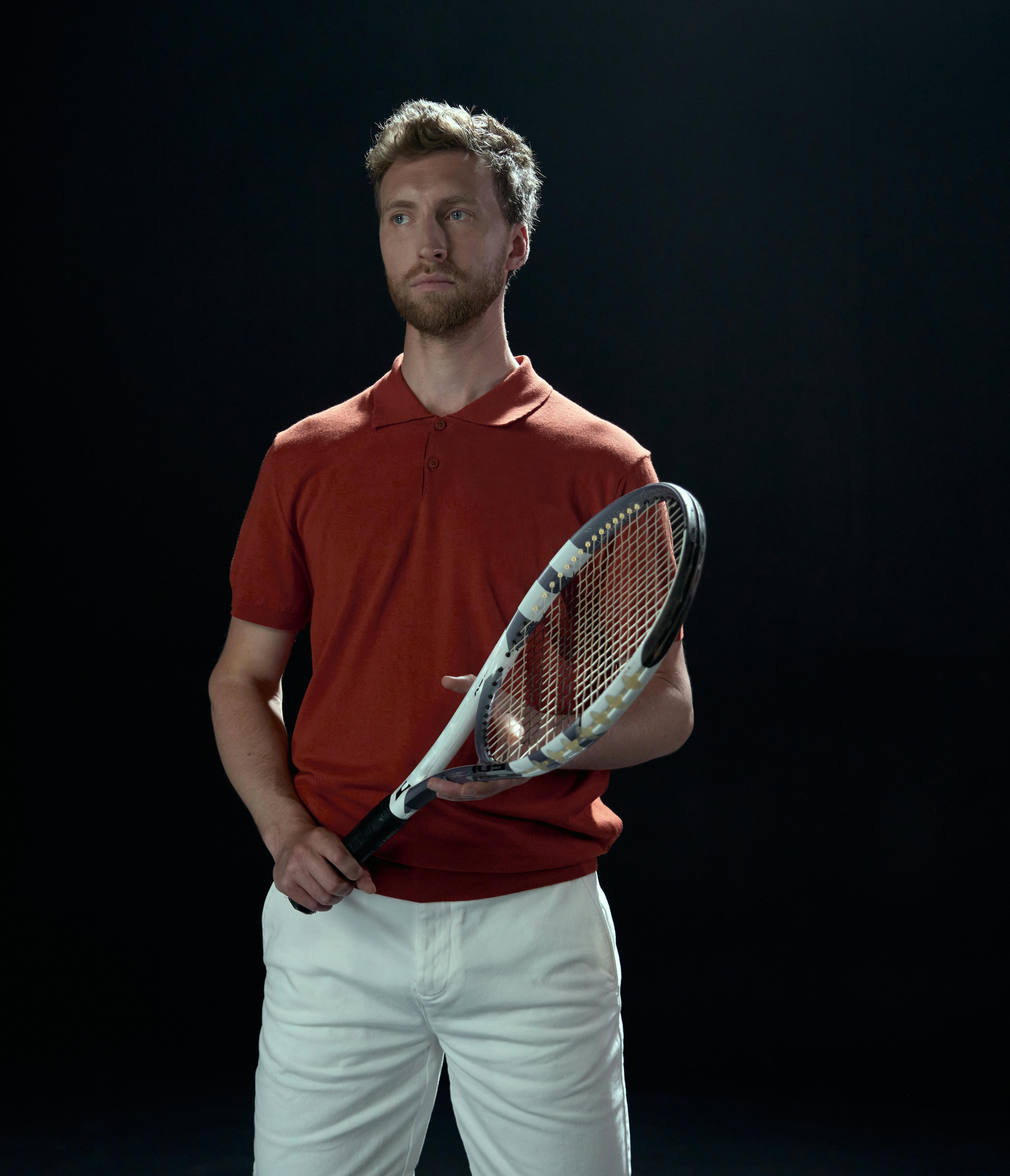 Portrait of a male tennis player holding a racket in a studio setting.