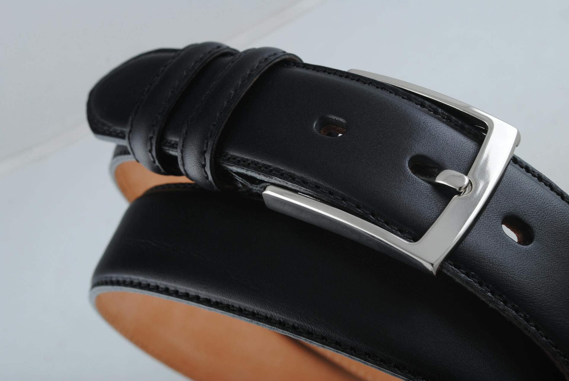 Detailed close-up of a stylish black leather belt featuring a shiny silver buckle, showcasing quality craftsmanship.