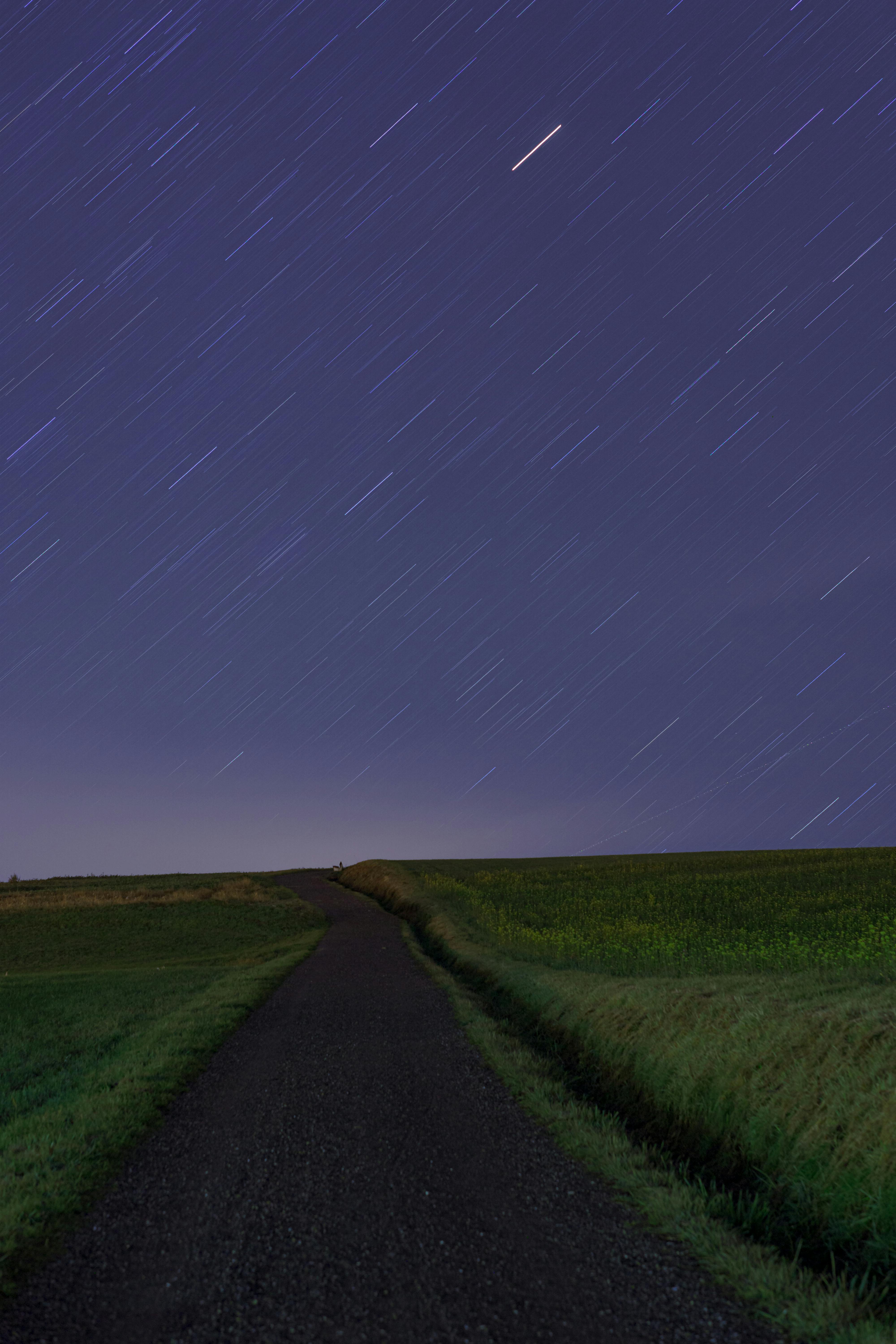 Captivating night sky with star trails over a quiet countryside road and fields.