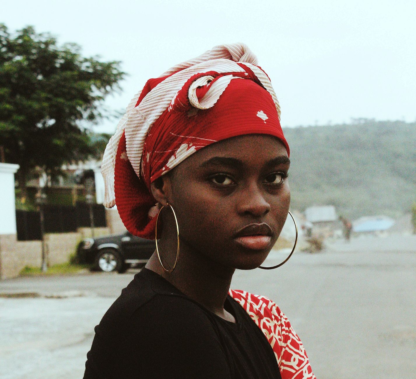 Stunning portrait of an African woman in Nigeria wearing a red headscarf and hoop earrings.