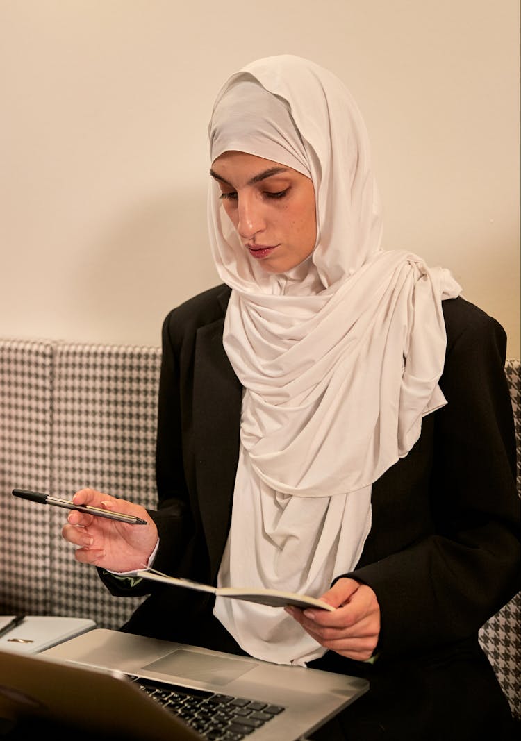 Young Muslim Woman In Hijab Sitting In Office And Reviewing Notes