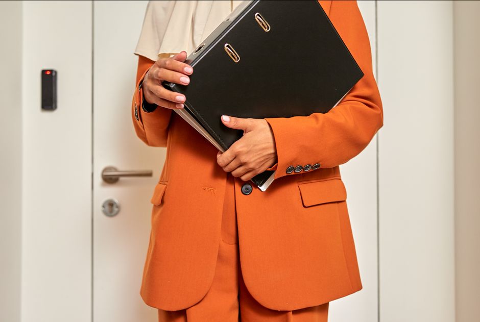 Un primer plano de una trabajadora de oficina sosteniendo un folder mientras está frente a una puerta cerrada.