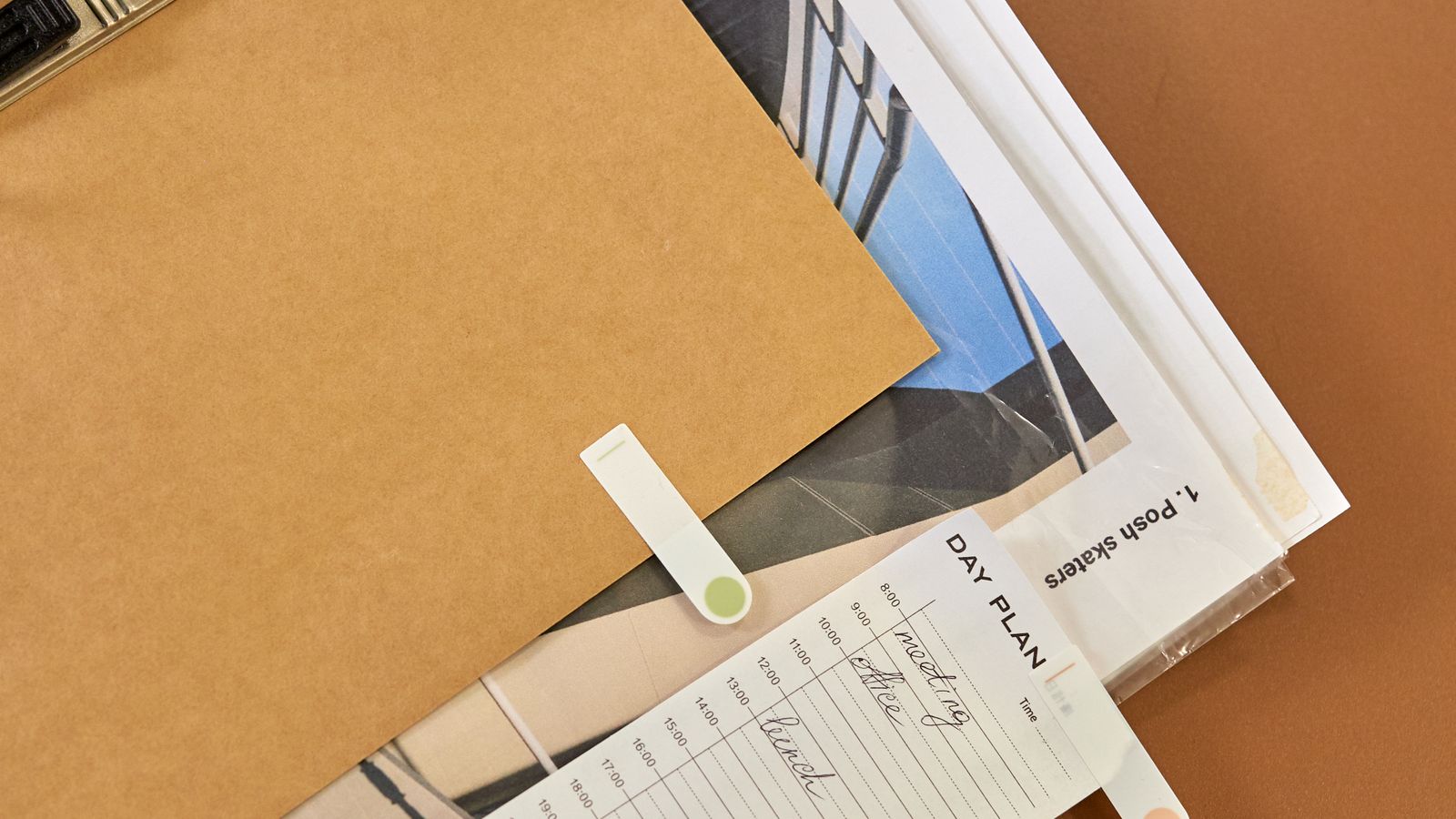 A clipboard, folder and day planner on a brown desk