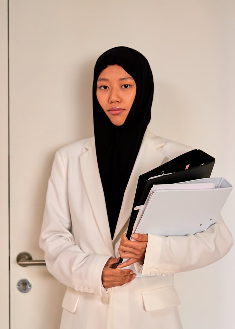 Young Muslim Woman Standing By Door With Documents In Hands