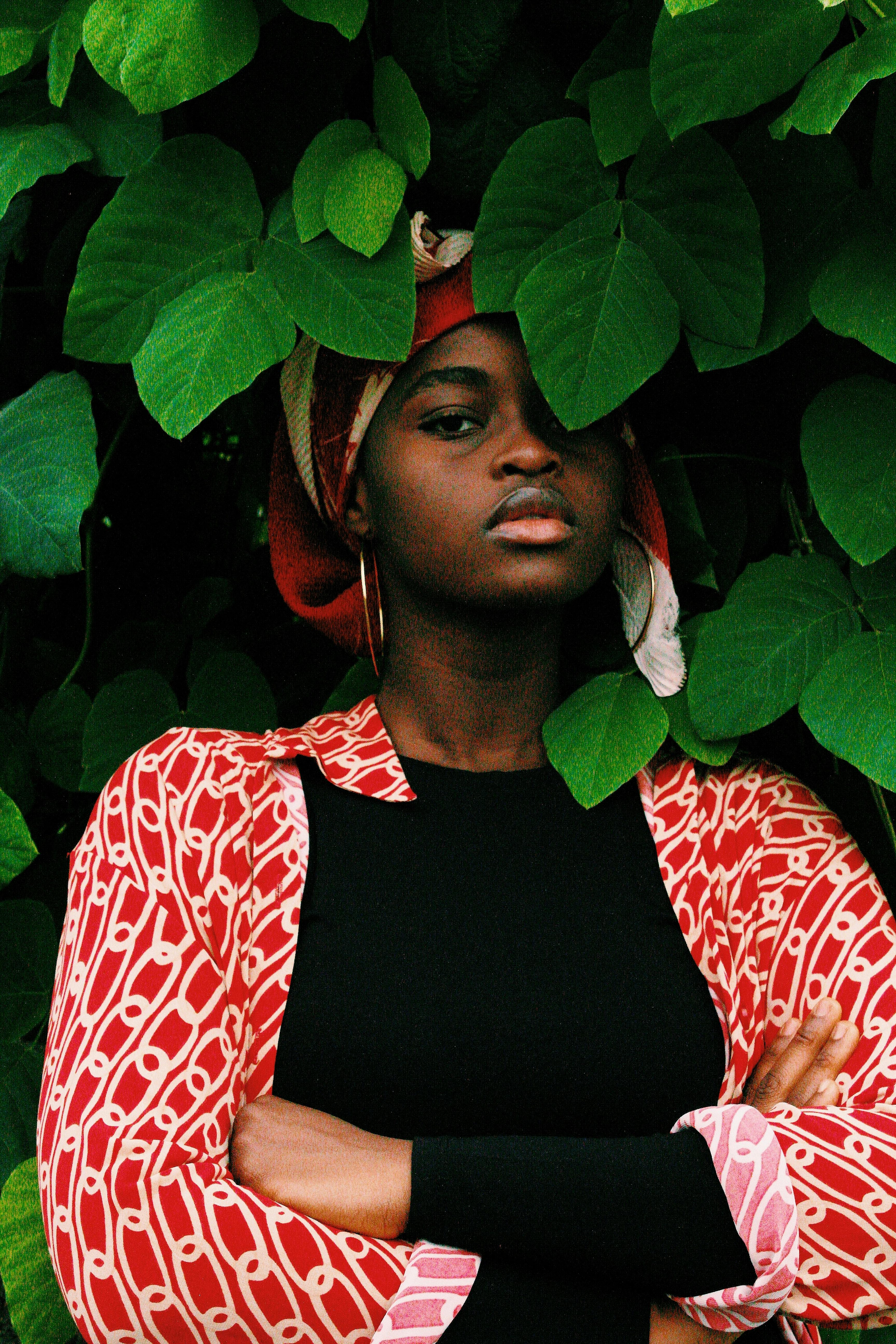 Striking portrait of a woman surrounded by lush green leaves, exemplifying natural beauty and style.