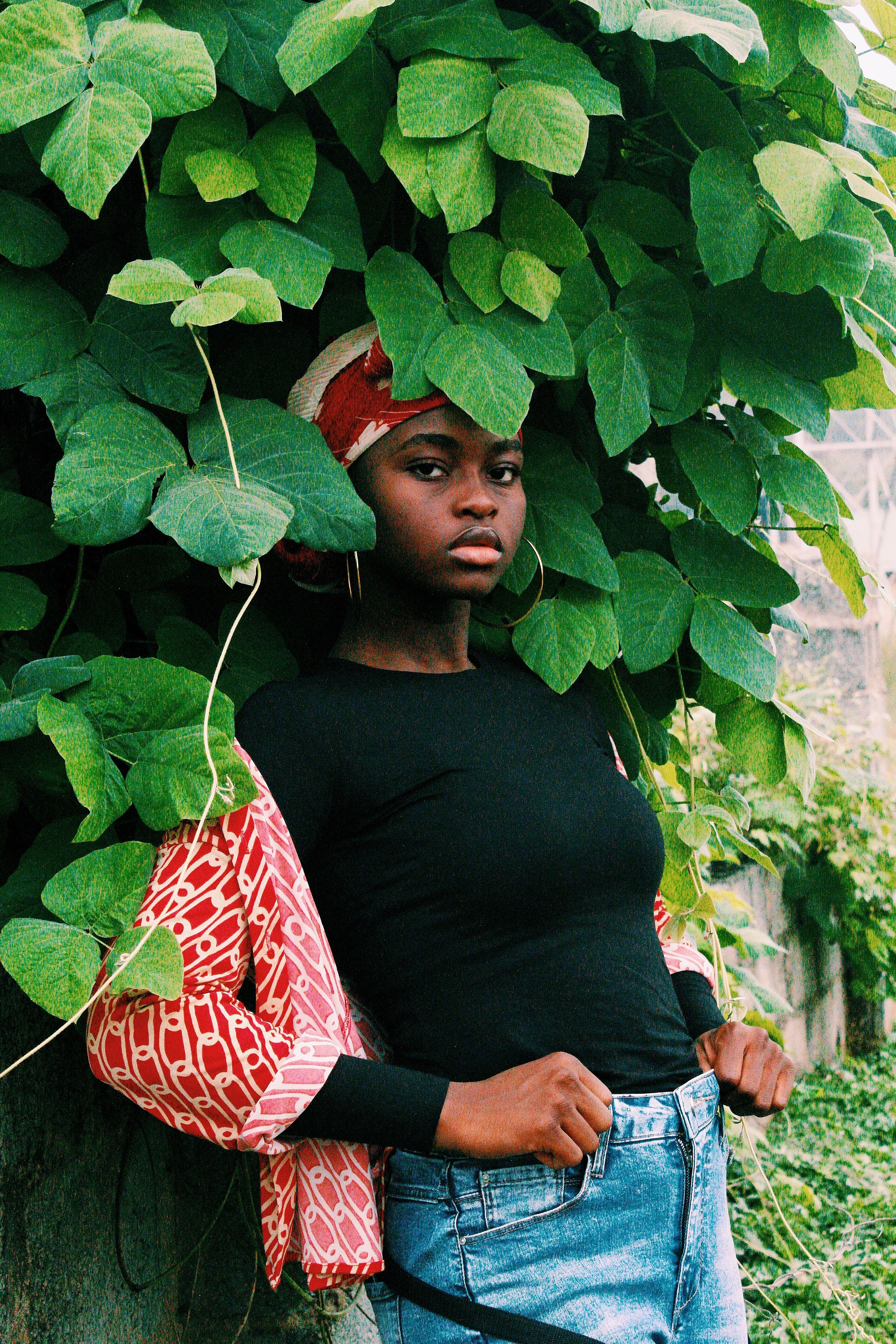 A fashionable woman poses outdoors amidst lush green leaves in Nigeria.