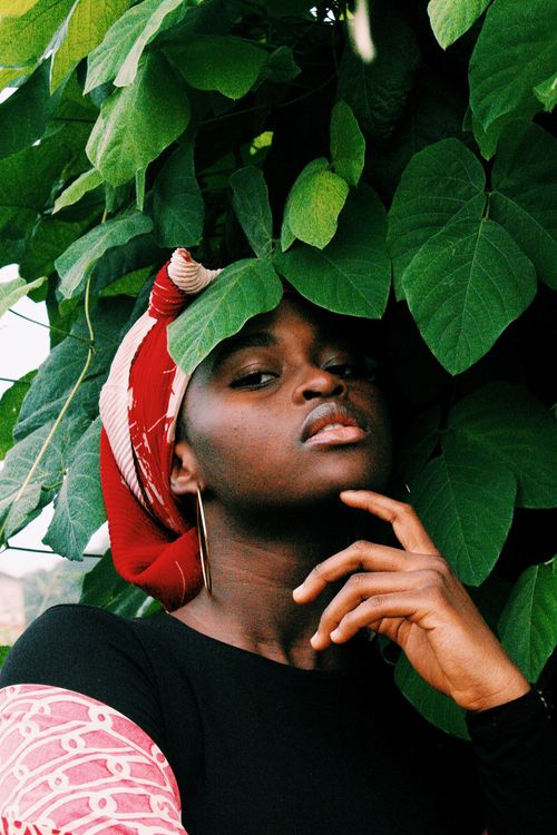 Free A striking portrait capturing a woman with a bright head wrap, surrounded by lush green leaves. Stock Photo