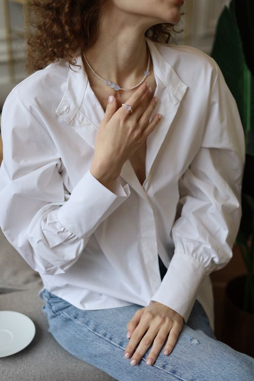 Free Close-up of a woman in a white shirt with jewelry, seated indoors. Stock Photo