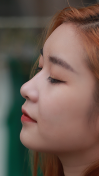 Close-up profile portrait of a young woman with long hair and makeup, eyes closed, serene expression.