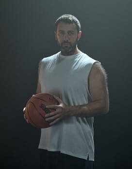 Bearded man in a tank top holding a basketball against a black background.