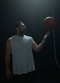 Adult male basketball player skillfully balancing a ball on finger in a dramatic studio setting.