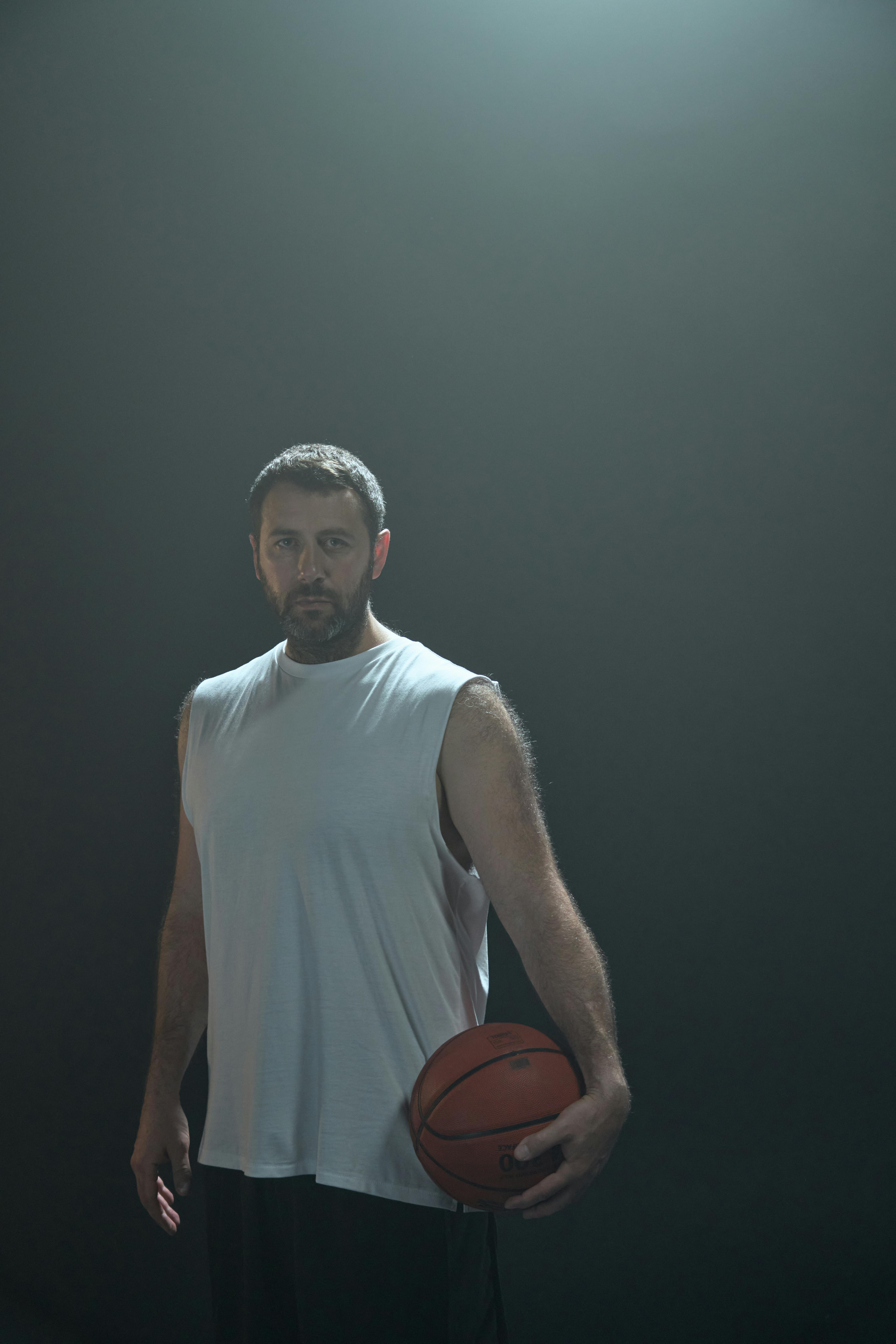 Focused athlete standing with basketball in a studio setting.