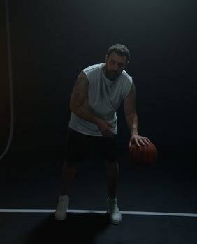 Man dribbling a basketball in a dimly lit studio setting, highlighting athleticism and focus.