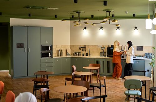 Free A stylish office breakroom with two colleagues in conversation, creating a professional and warm atmosphere. Stock Photo