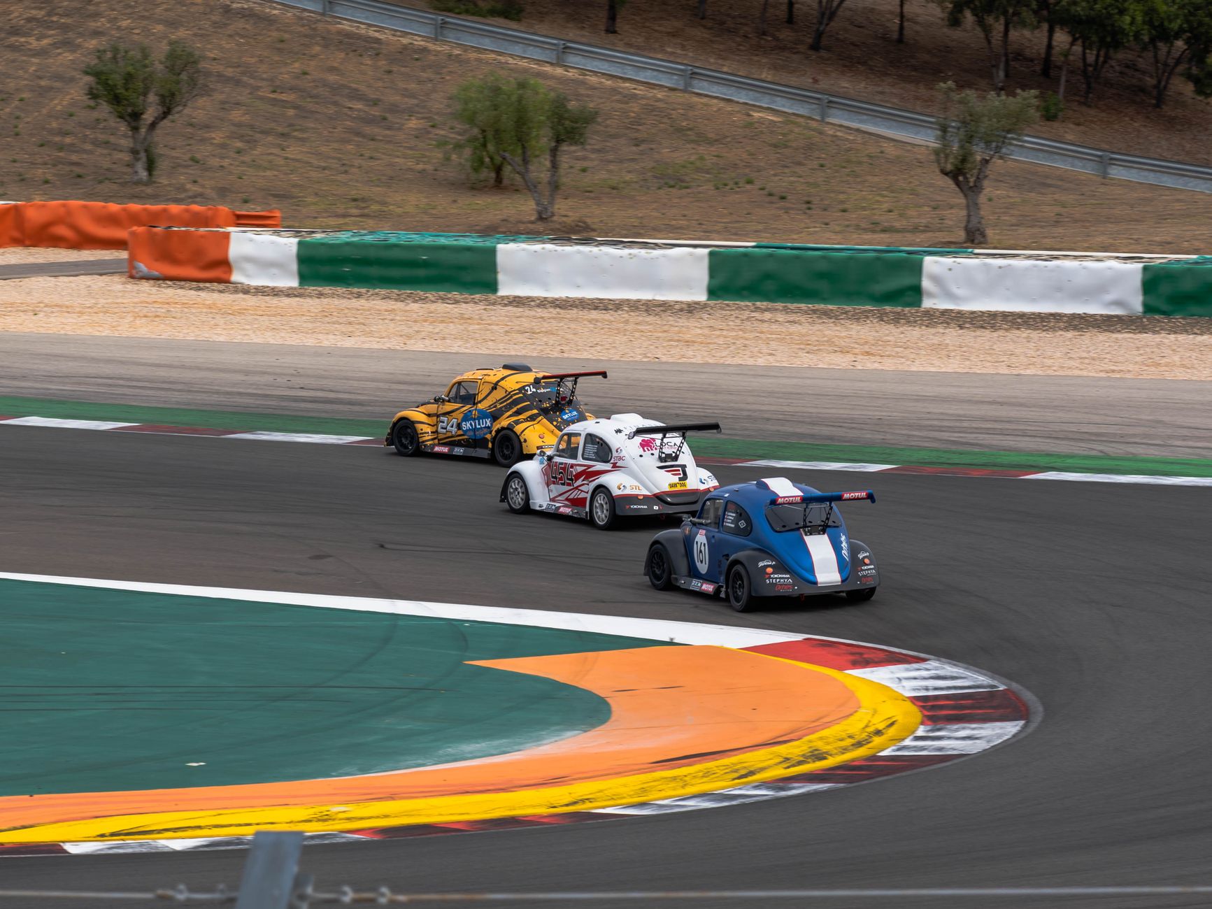 Volkswagen Beetles racing on a colorful, challenging racetrack curve under a clear sky.