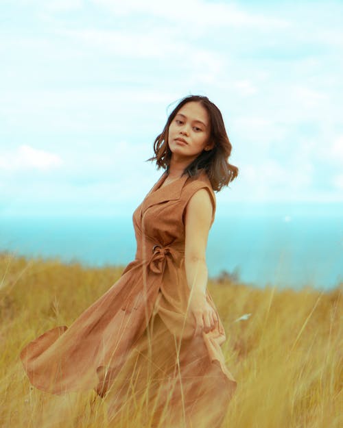 Woman in Brown Sleeveless Dress Standing on Grass Field