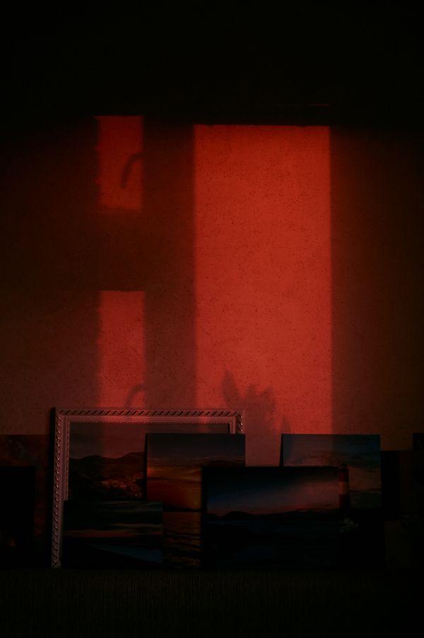 Red window light on a wall behind stacked framed prints, photo by Amina B on Pexels