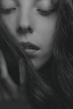 Close-up black and white portrait of a woman with closed eyes and hand touching hair.