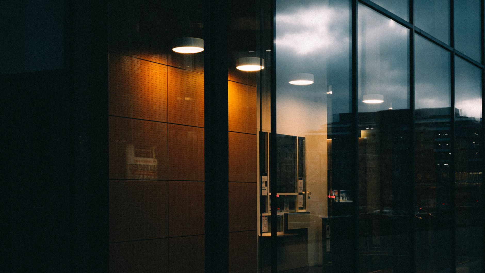 A modern building showcasing warm interior lights and evening sky reflections on its glass facade.