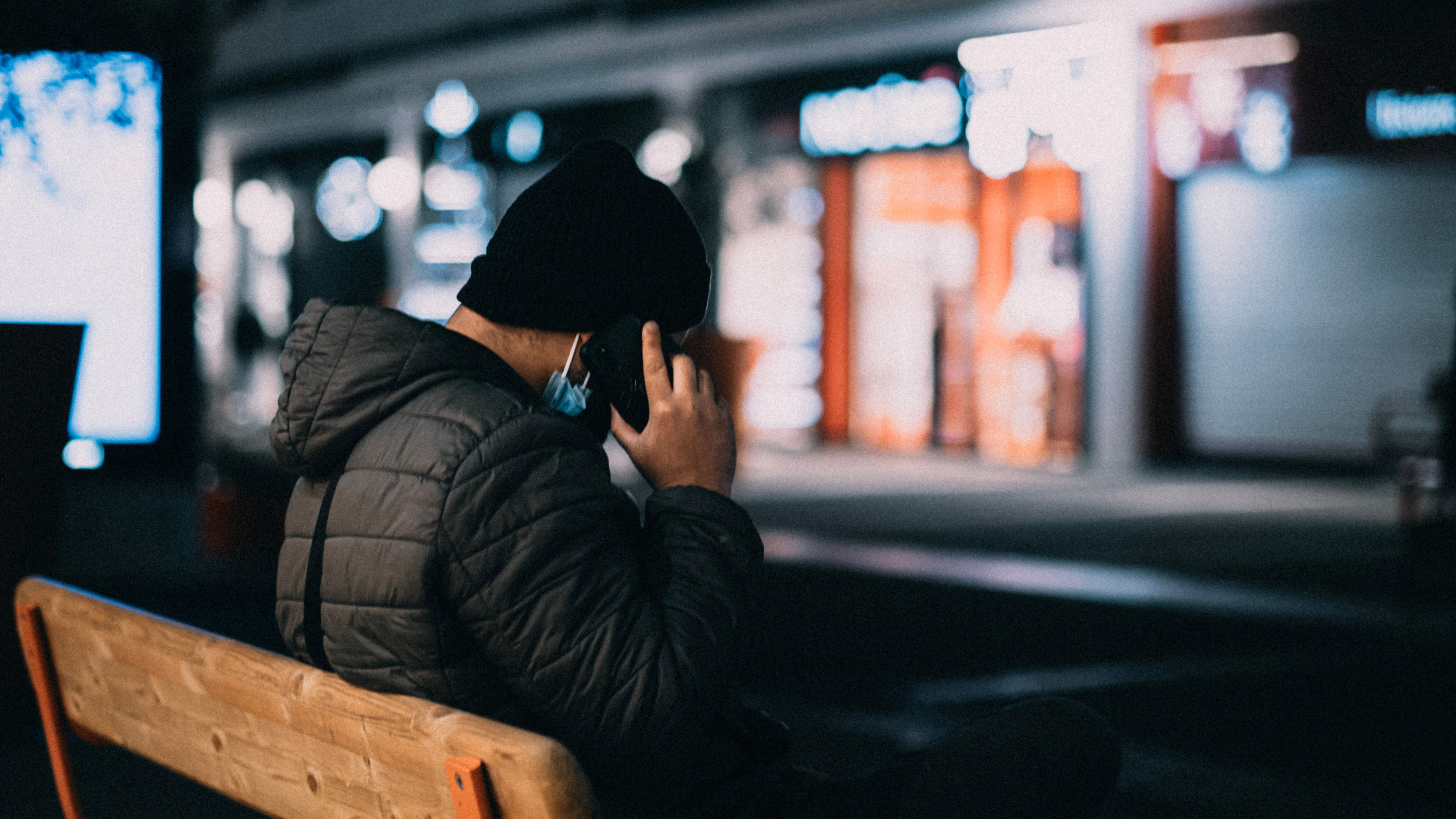 Man in a winter jacket making a phone call on a bench at night, creating a moody, urban atmosphere.