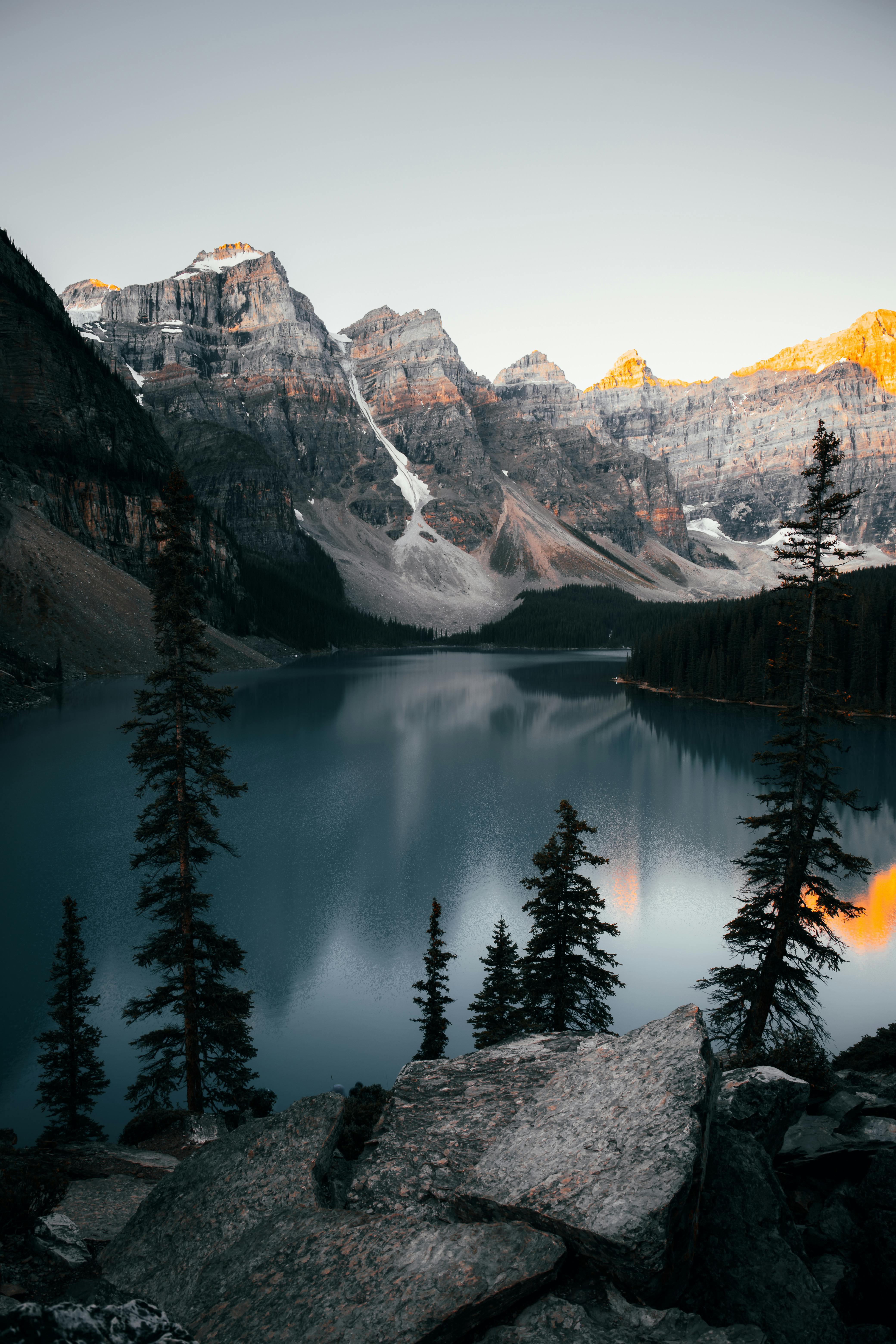 A breathtaking view of Moraine Lake with snowy peaks and pine trees during sunset in Banff National Park, Alberta, Canada.