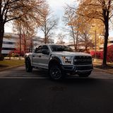 A modern pickup truck parked on a city street surrounded by autumn trees.