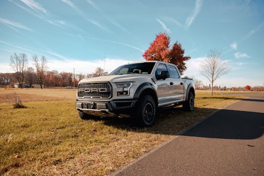 A Ford pickup truck parked beside an empty country road during autumn with colorful foliage.