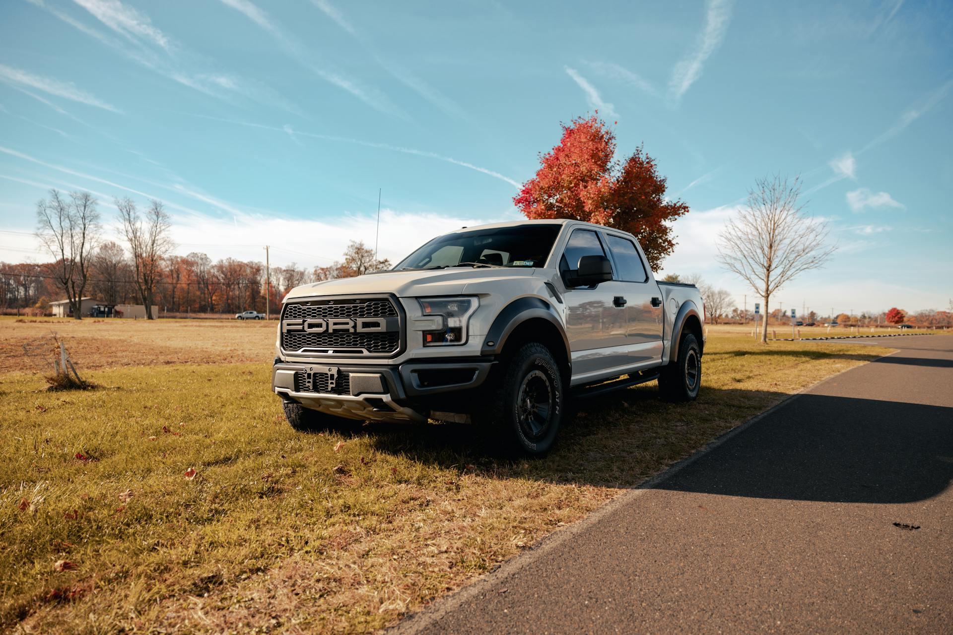 A Ford pickup truck parked beside an empty country road during autumn with colorful foliage.