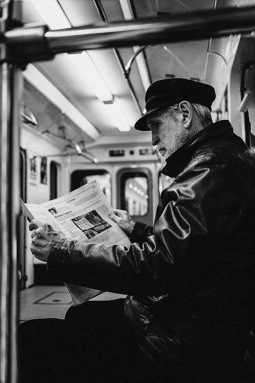 Man in Black Jacket Reading Newspaper Inside a Train