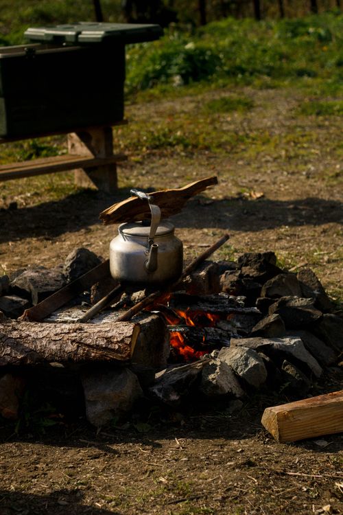 Free A kettle boils over a campfire surrounded by rocks in a natural outdoor setting. Stock Photo