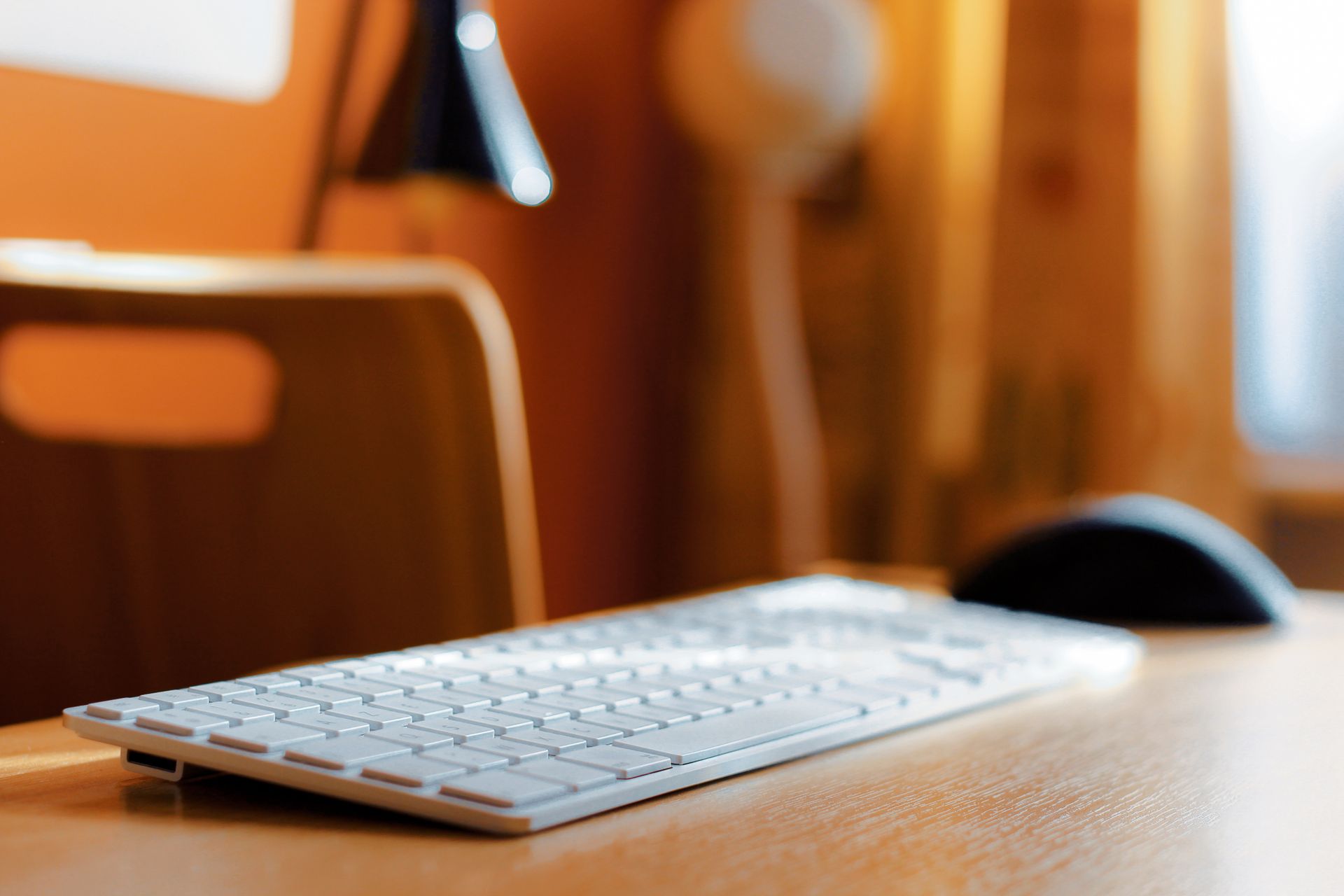 Sleek close-up of a keyboard and mouse on a wooden desk in a modern workspace setting.