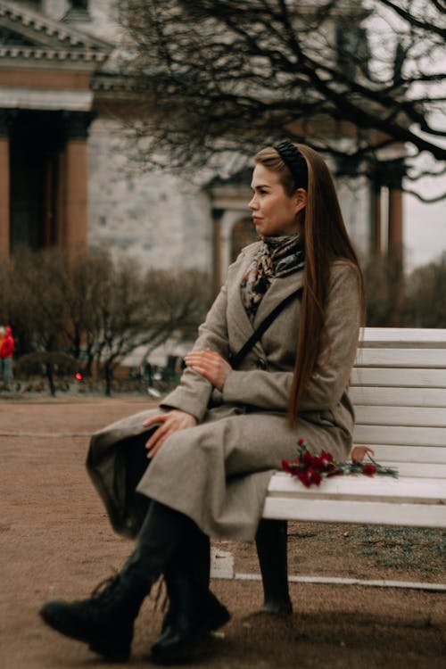 A Woman in Gray Coat Sitting on White Bench