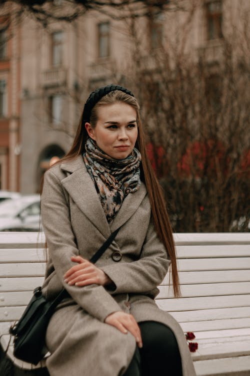 A Woman in Brown Coat Sitting on a Wooden Bench