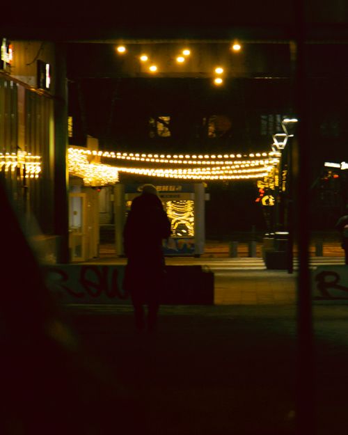 Free A moody nighttime street scene featuring silhouetted figures under illuminated street lights. Stock Photo