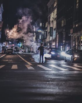 Vibrant city night scene with smoke and cars on a bustling urban street.