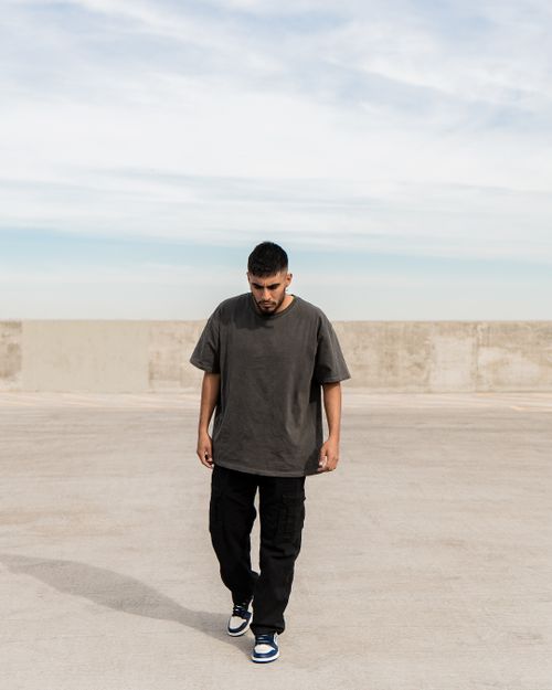 Free A man stands pensively on a rooftop, wearing casual black clothing under a clear sky. Stock Photo