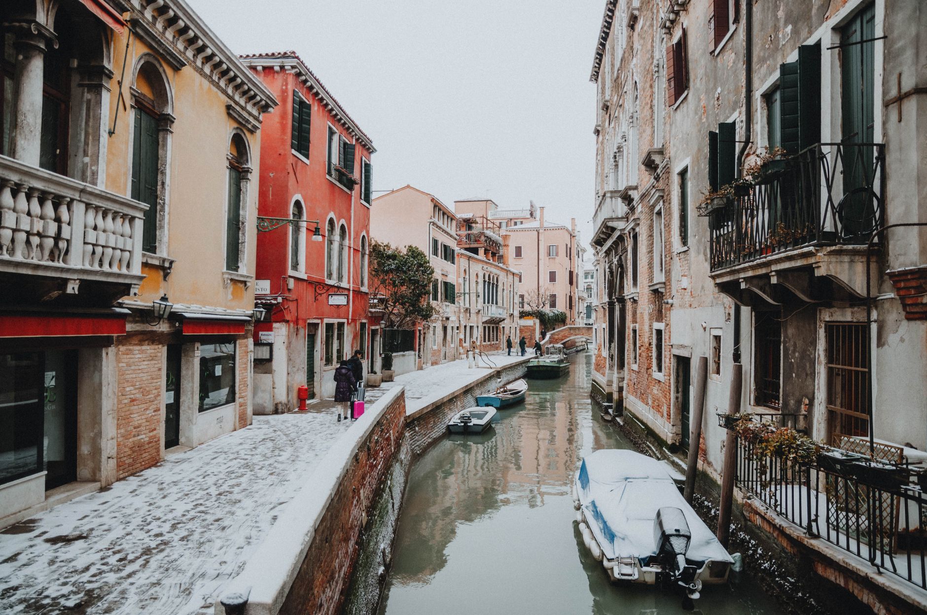 Snow-dusted Venetian canal with colorful buildings and boats reflecting serene winter atmosphere.
