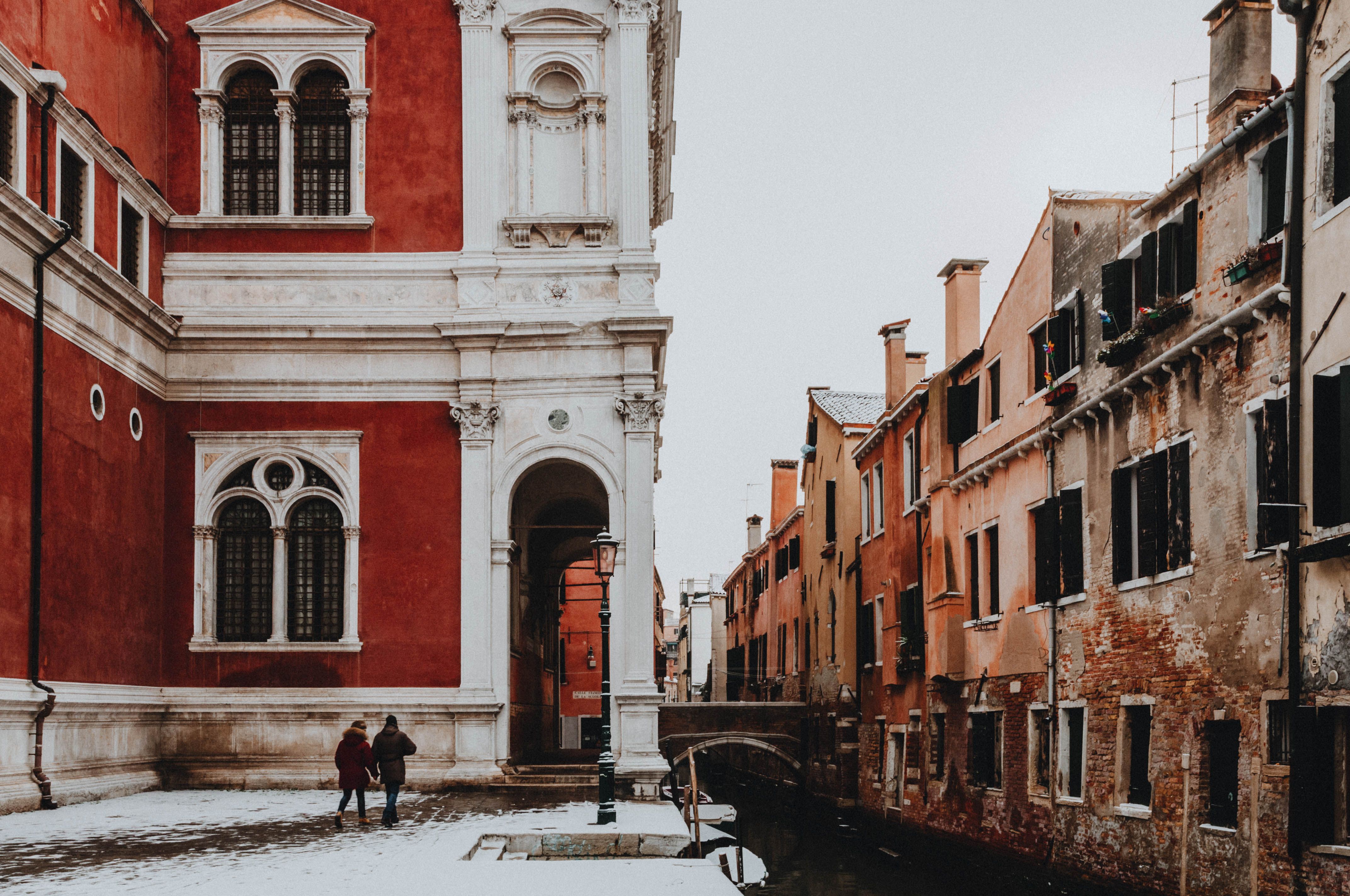 Snow along a narrow canal in Venice beside a red palazzo