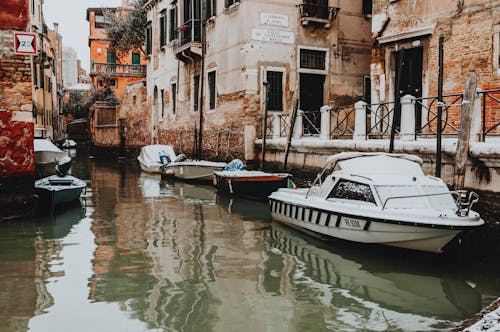 White and Blue Boat on River Between Concrete Buildings