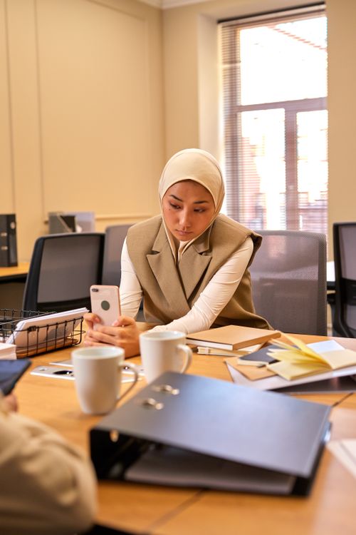 Free Woman in a professional setting using a smartphone at her desk with office supplies around. Stock Photo