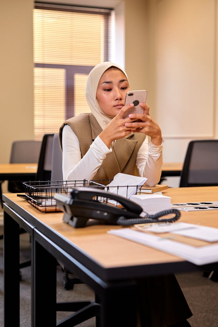 Young Muslim Woman Sitting At Office Desk And Texting On Smartphone