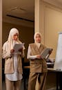 Two Females in Hijab Standing in Office Room and Holding Documents in Hands
